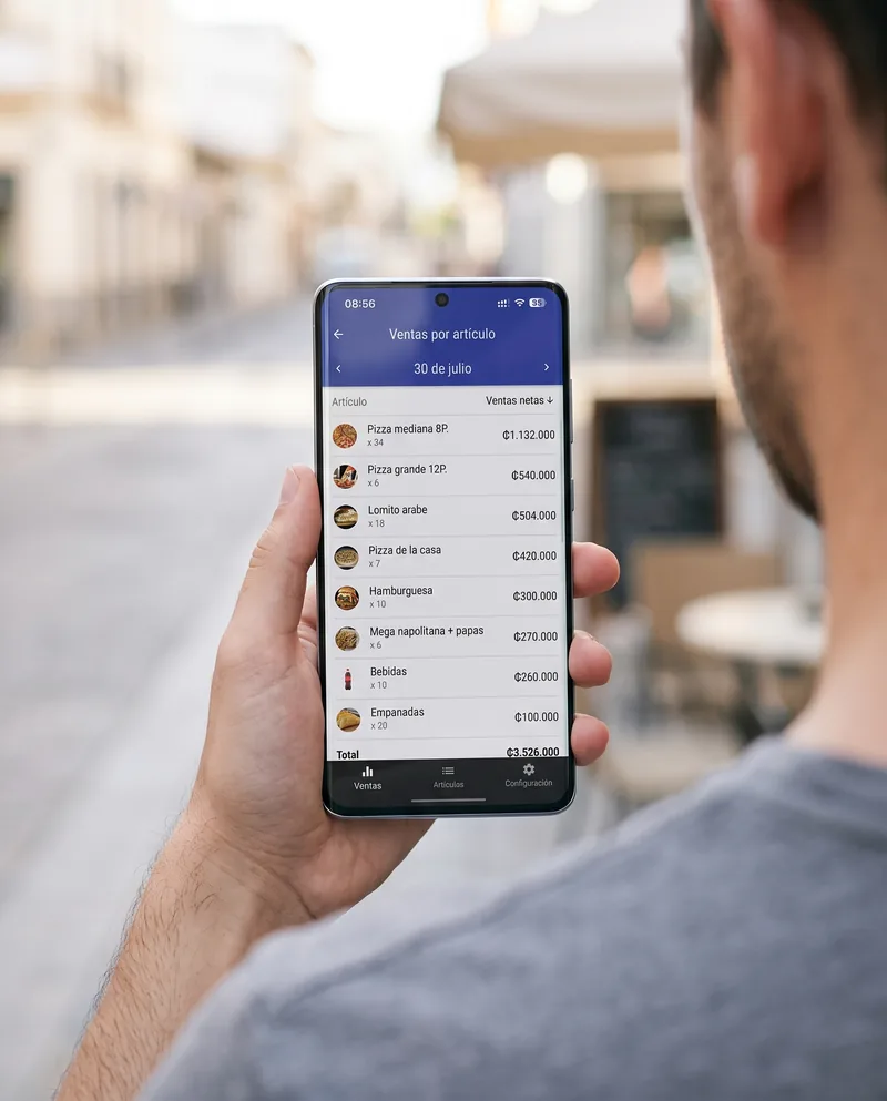 Fuera del local, de mañana: el celular muestra las ventas por artículo del día, ordenadas de mayor a menor, con las cantidades vendidas.